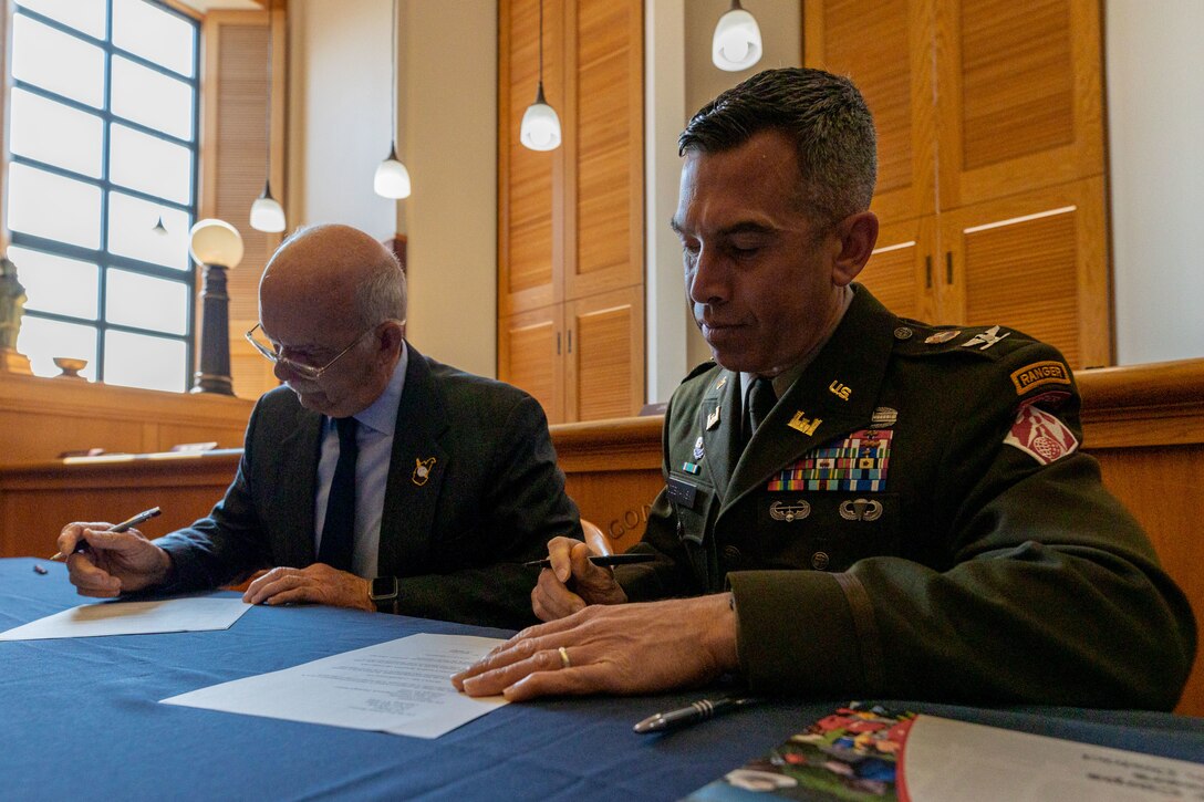 Two men sitting at a table signing papers.