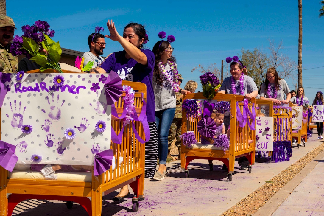 People push children in cribs with wheels down a sidewalk.