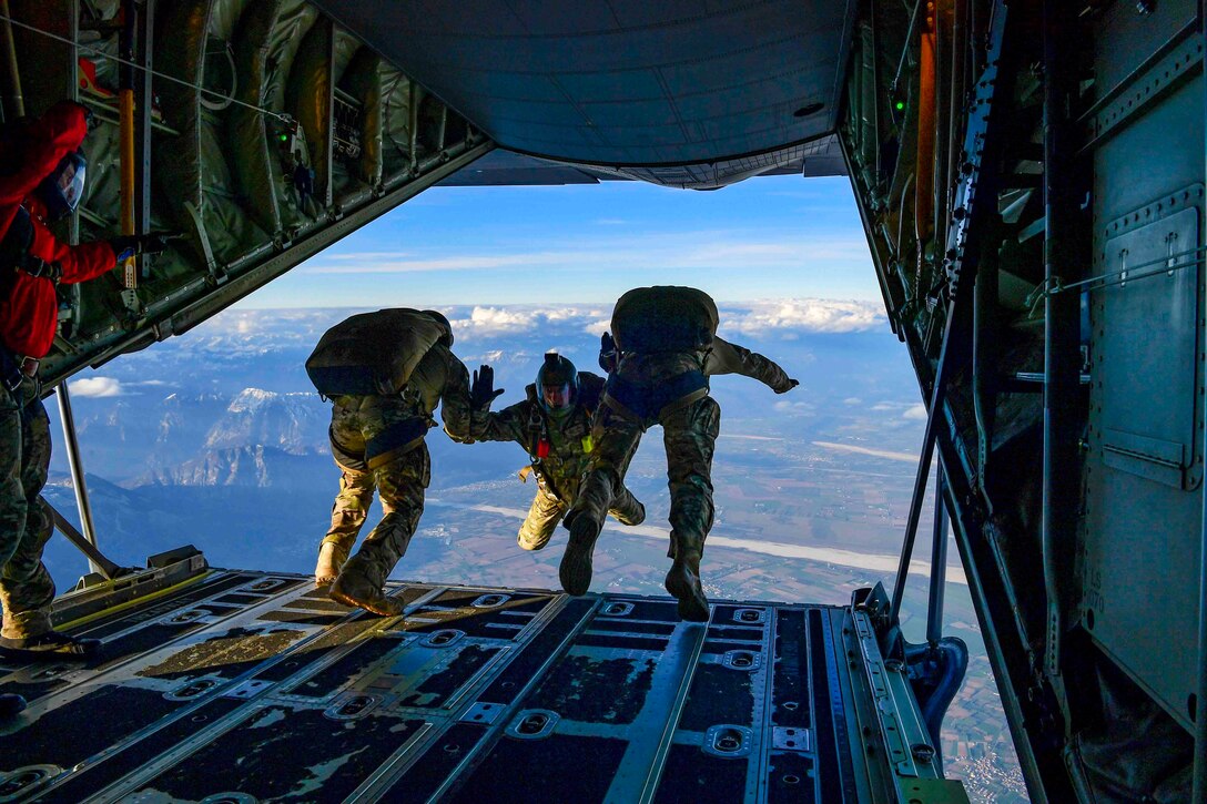 Three airmen jump out of an airborne aircraft.