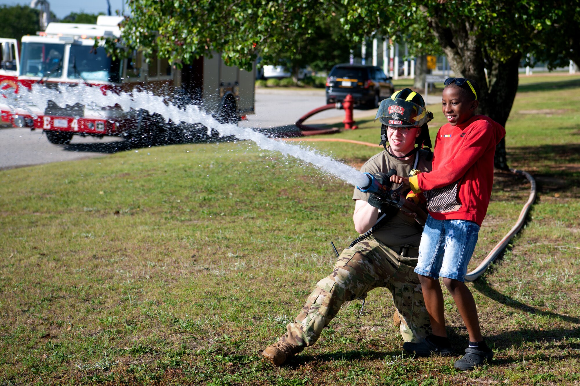 U.S. Air Force Airman 1st Class Logan Smith, 20th Civil Engineer Squadron (CES) firefighter, helps a student aim a fire hose during a combined Earth Day and Career Day event at High Hills Elementary School, Sumter, S.C., April 21, 2023. The 20th CES spearheaded the partnership with High Hills, putting on the event for 430 students for the second year in a row. (U.S. Air Force photo by Staff Sgt. Kelsey Owen)
