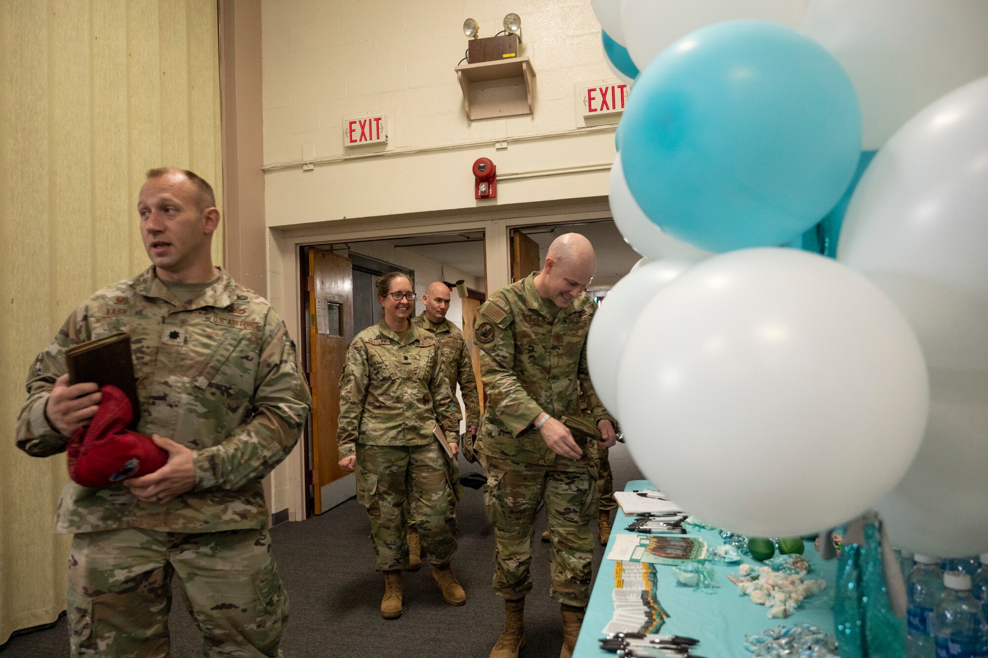 People in uniform sign in at a table with white and teal balloons.