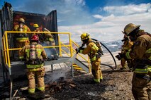 Deputy Fire Chief Ryan Tworek, with Fire and Emergency Services, works with firefighters to reset the Drager Phase 1 System, before the next rotation of firefighters enter the system to recreate more fire and smoke behaviors during training aboard Marine Corps Logistics Base Barstow, California, March 30. The firefighters would douse the old wood and coals, then reload the Drager system with new wood, closing it up, then stoking the fresh wood into flames using a torch. The vents on the top and back, as well as the doors, are used to control the amount of air the fire gets, in order to manipulate the fire and smoke behaviors. This allows firefighters to experience real-life hazardous  events, such as full burn-overs, and zero visibility, in a safe and controlled environment.