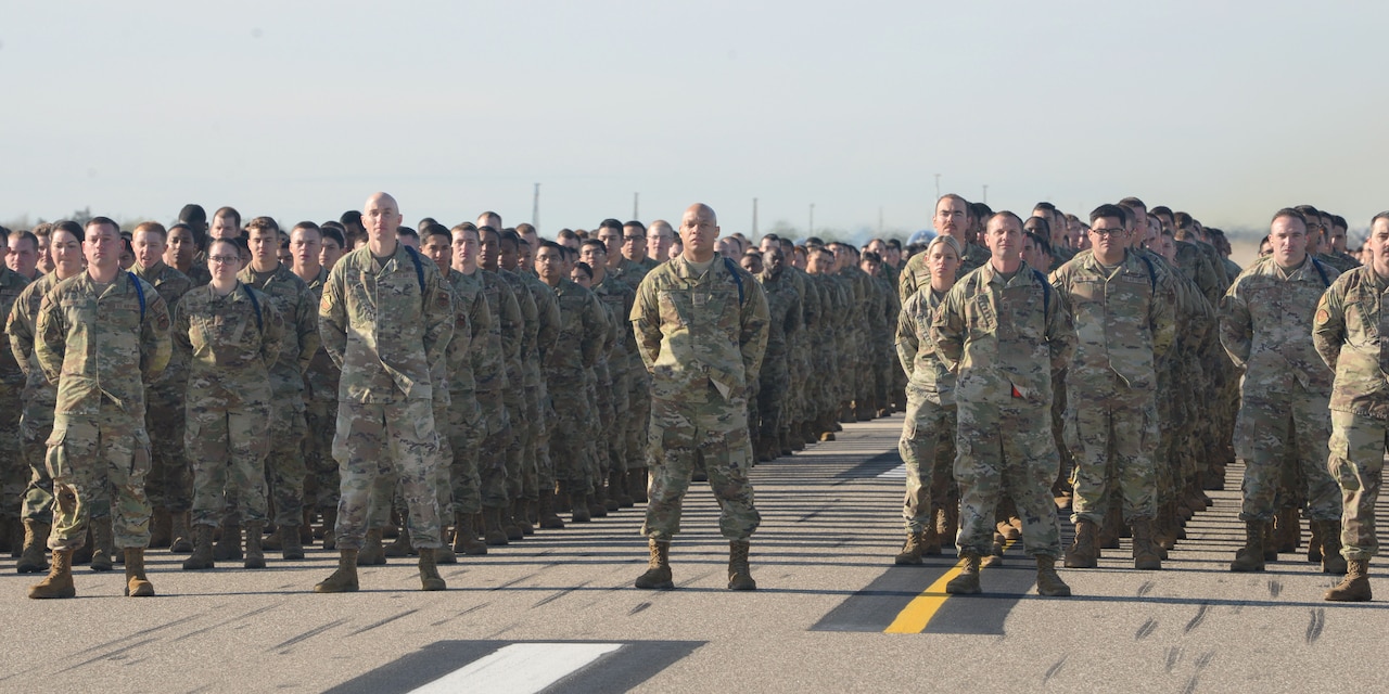 Wide shot showing dozens of airmen standing in formation on a runway.