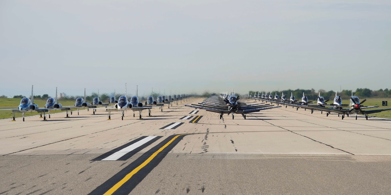 Wide view of dozens of aircraft in formation on a runway.