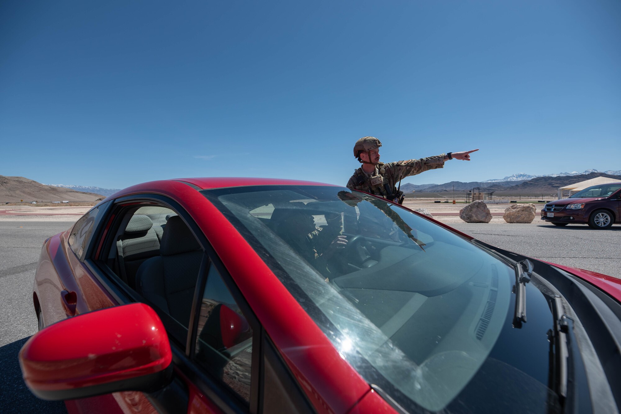 A man in uniform points while standing next to a red vehicle; the vehicle driver is also in uniform.