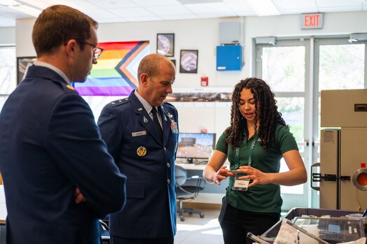  U.S. Space Force Maj. Matthew Masters, Combined Force Space Component Command (CFSCC) Commander's Action Group deputy chief, left, and U.S. Space Force Maj. Gen. Douglas A. Schiess, CFSCC commander, middle, listen to Kayla Del Rosario, California Polytechnic State University mechanical engineer student, as she explains some of the materials she uses for CubeSat satellite projects at California Polytechnic State University in San Luis Obispo, Calif., April 25, 2023. The Cal Poly CubeSat Laboratory is part of PolySat, a student-run, multidisciplinary independent research lab at the university which partnered with Vandenberg through a Cooperative Research and Development Agreement (CRADA) in 2019, the first of its kind between the base and an academic institution. A CRADA is a no-cost collaboration that enables the transfer and exchange of technology and professional expertise. (U.S. Space Force photo by Tech. Sgt. Luke Kitterman)