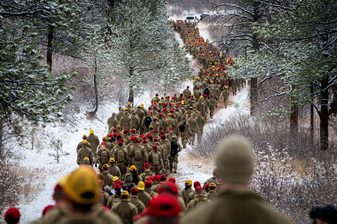 A long line of Air Force cadets walk through snowy woods.