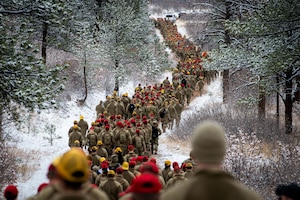 A long line of Air Force cadets walk through snowy woods.