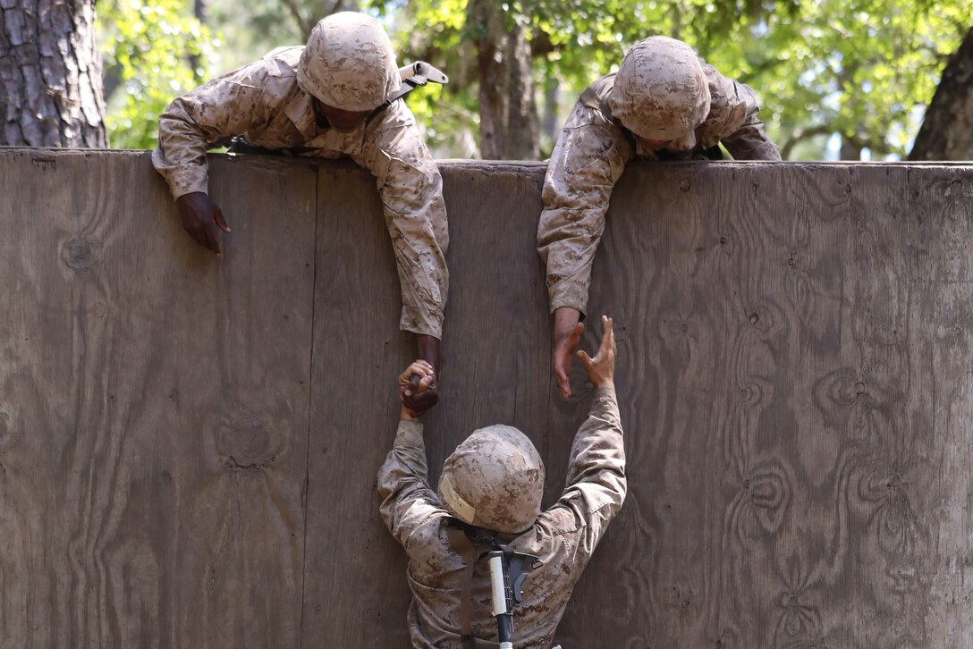 Marine Corps recruits help lift another up a wall.