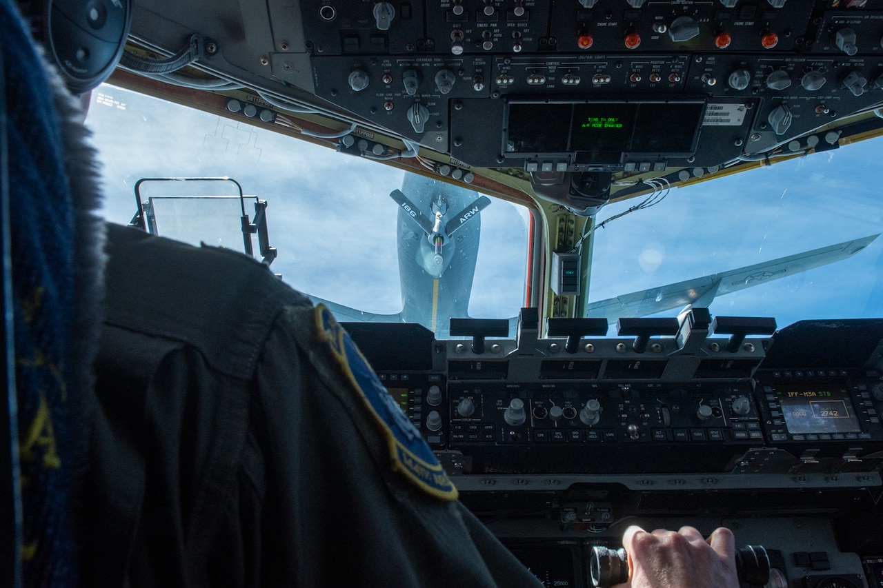 A pilot operates cockpit instruments while following close behind another aircraft.