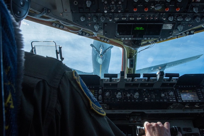 A pilot operates cockpit instruments while following close behind another aircraft.