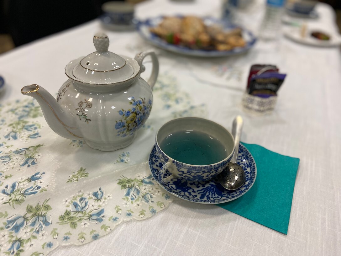 Tea pot with tea cup filled with teal-colored tea.