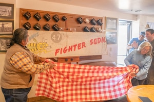 Art Conservators Timothy Lewis and Matilde Rubio, Tohono Restoration, pose in front of the 47th Fighter Squadron flag they restored and unveiled to the unit at the 47th FS clubhouse at Davis-Monthan Air Force Base, Ariz., March 3, 2023. Lewis and Rubio were chosen to restore the World War II era 47th FS flag after a WWII 47th FS alum noticed it hanging in the unit during a tour. The alum shared the historical significance of it and donated the fund to get it protective for life. (U.S. Air Force photo by Staff Sgt. Tyler J. Bolken)