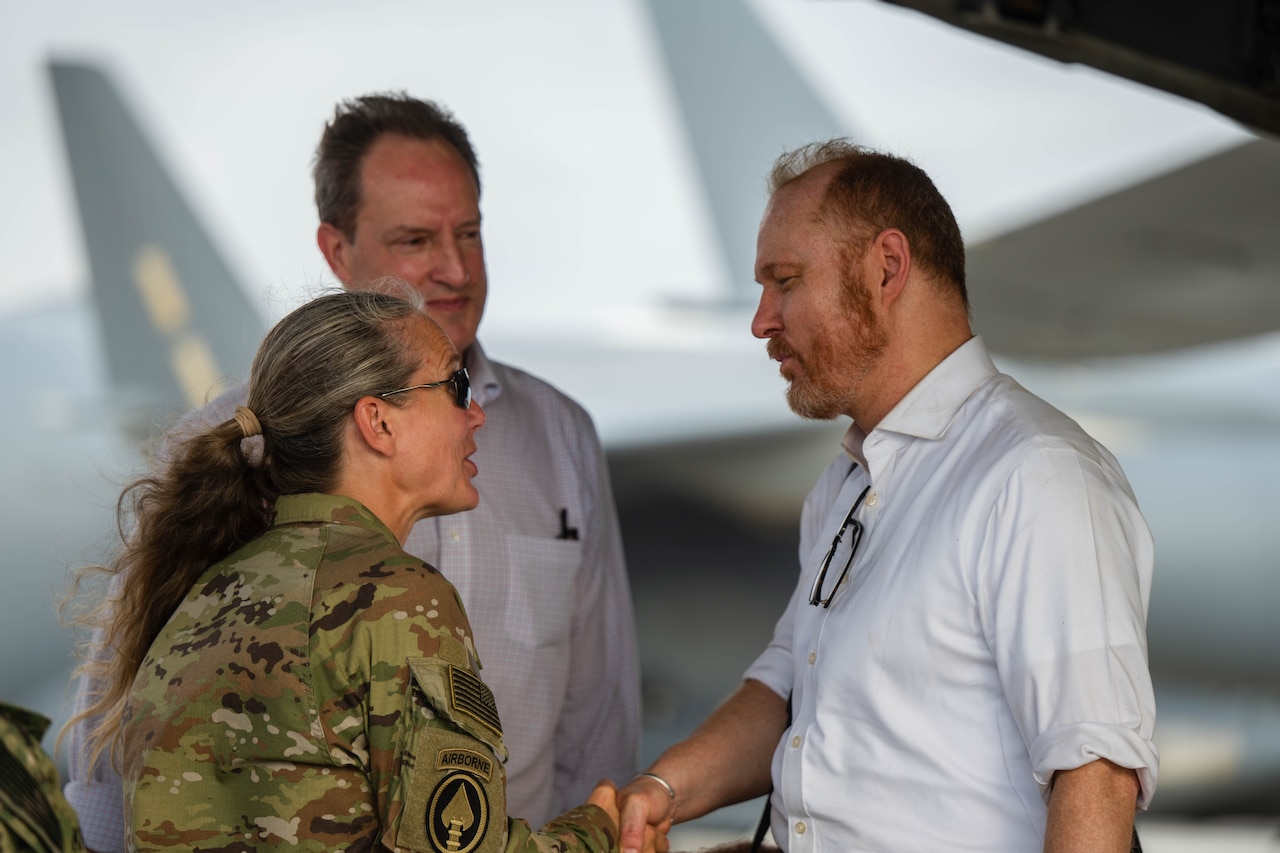 A woman in uniform shakes hands with a man in civilian attire. Another man looks on.