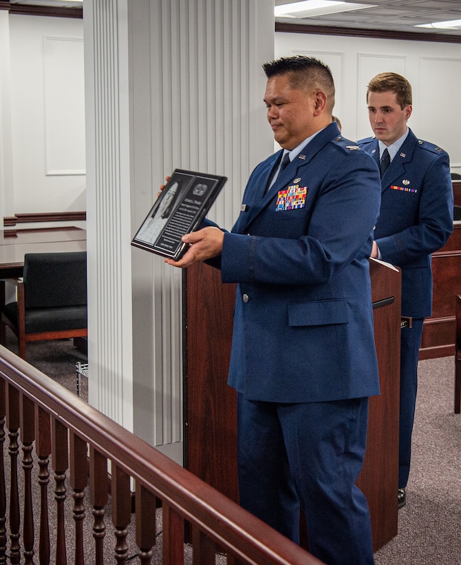 U.S. Air Force Col. Brian Banas, 673d Air Base Wing Judge Advocate staff judge advocate, displays a memorial plaque to gathered coworkers and friends of Kimberly Pfender, a retired U.S. Air Force master sergeant, during a 673d ABW/JA courtroom dedication at Joint Base Elmendorf-Richardson, Alaska, April 6, 2023. Pfender served with distinction as both an Air Force non-commissioned officer and civil servant for a combined federal service of 28 years. (U.S. Air Force photo by Tech. Sgt. Curt Beach)