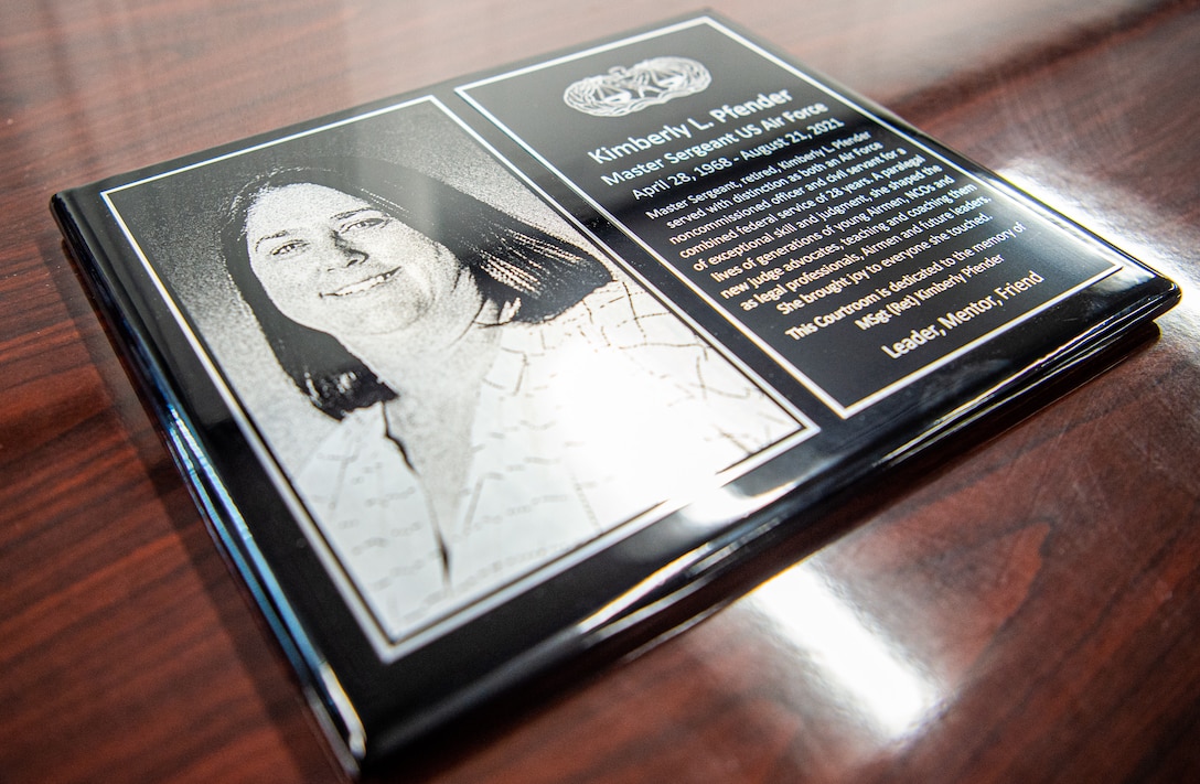 A memorial plaque honors Kimberly Pfender, a retired U.S. Air Force master sergeant, during a 673d Air Base Wing Judge Advocate courtroom dedication at Joint Base Elmendorf-Richardson, Alaska, April 6, 2023. Pfender served the U.S. Air Force in active duty and civil service for 28 years and passed away Aug. 21, 2021. The plaque reads: “Master Sergeant, retired, Kimberly L. Pfender served with distinction as both a non-commissioned officer and civil servant for a combined federal service of 28 years. A paralegal of exceptional skill and judgment, she shaped the lives of generations of young Airmen, NCOs and new judge advocates, teaching and coaching them as legal professionals, Airmen and future leaders. She brought joy to everyone she touched. This courtroom is dedicated to the memory of MSgt (Ret) Kimberly Pfender. Leader, Mentor, Friend.” (U.S. Air Force photo by Tech. Sgt. Curt Beach)