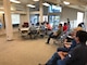 Eleven adults are sitting in metal chairs in a small, carpeted room with a pitched ceiling and windows. The people are all facing one direction looking at screen.