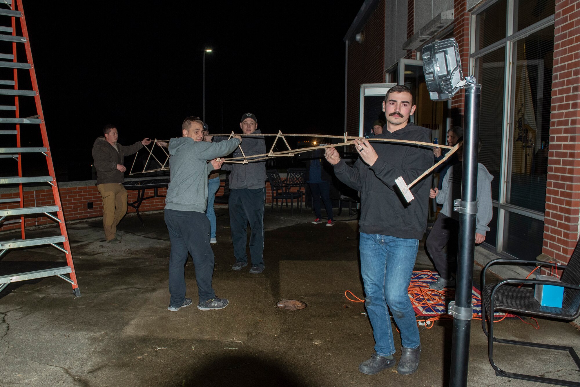 Volunteers carry the completed spire of a popsicle-stick structure.