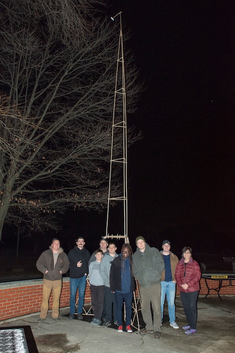 Volunteers stand in front of a completed 27-foot popsicle-stick structure.