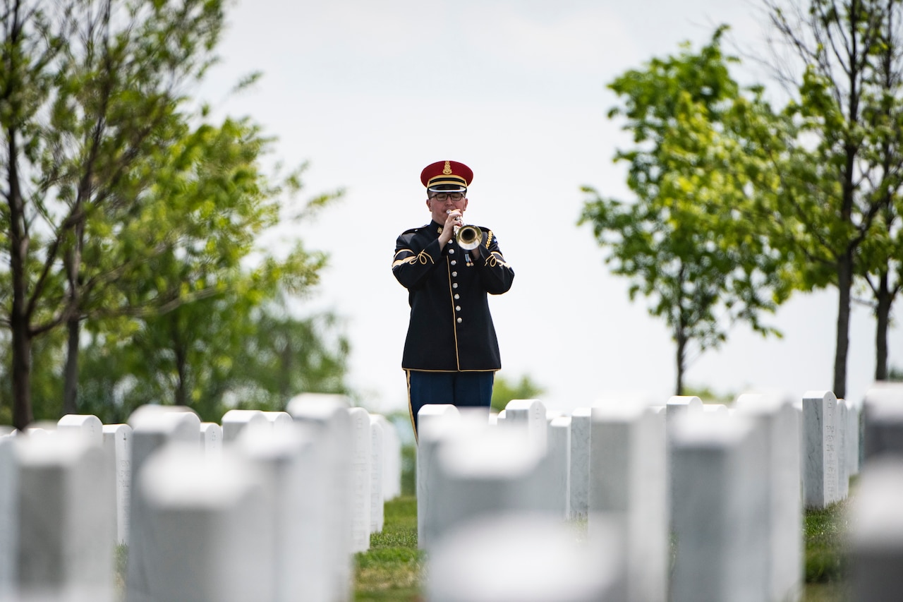 A service member plays a trumpet in a cemetery.