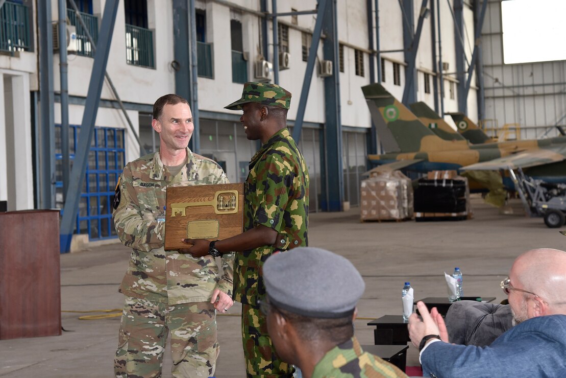 A man receives a plaque from another man; both are in military uniforms
