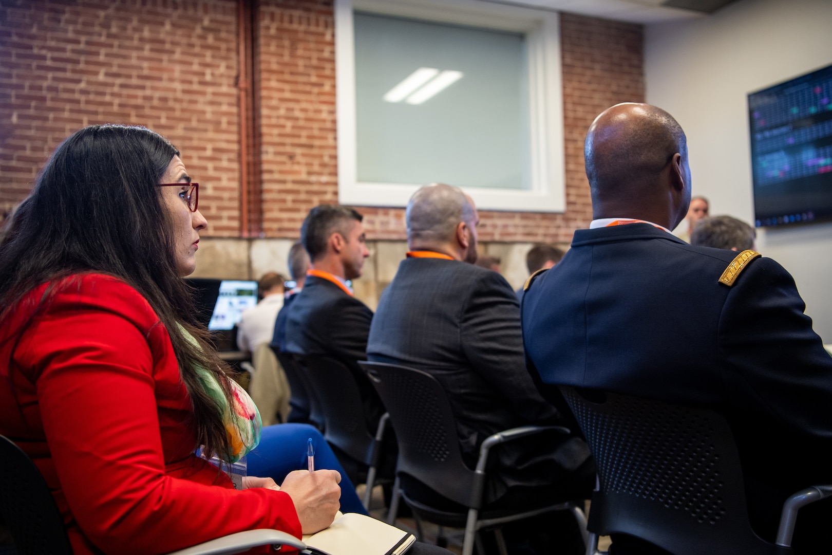 Woman in red suit looking at screen and taking notes