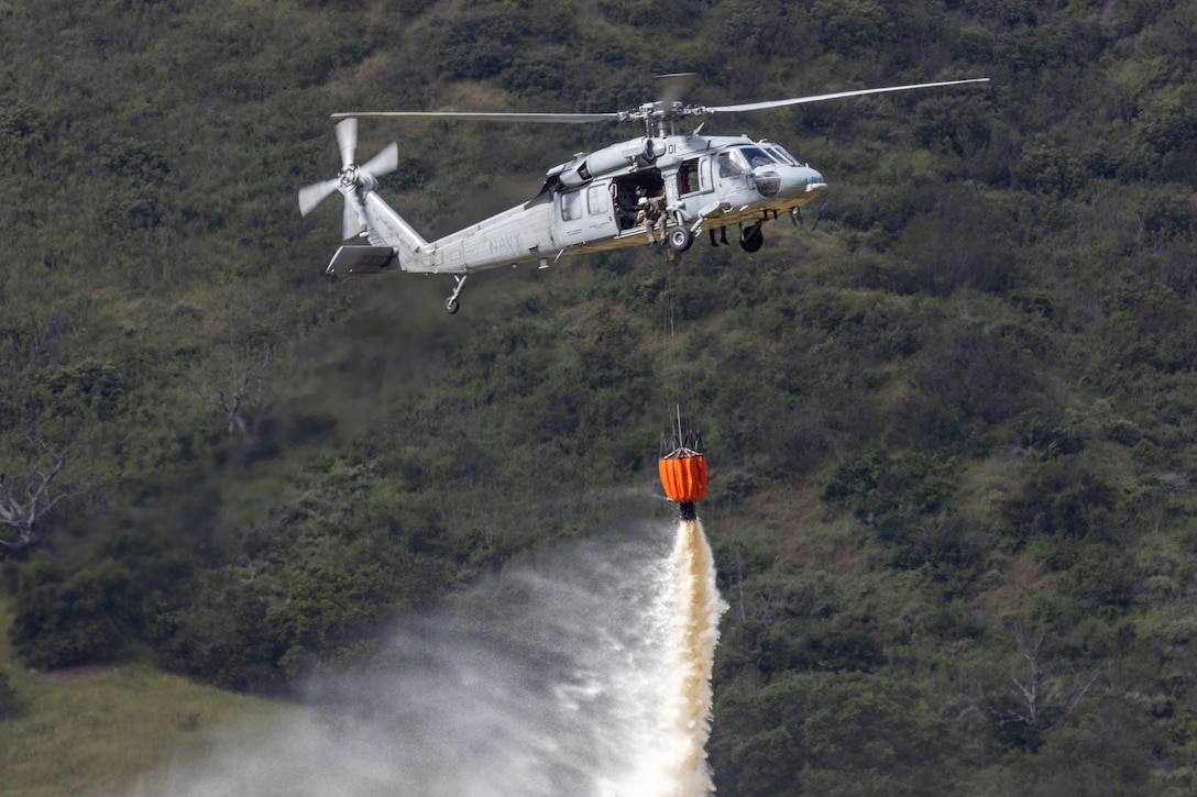 A helicopter drops water from a bambi bucket.