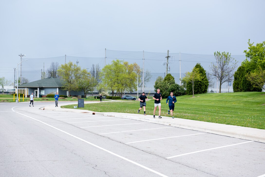 Several runners, men and women in fitness attire run on a street next to the green grass of a golf course.