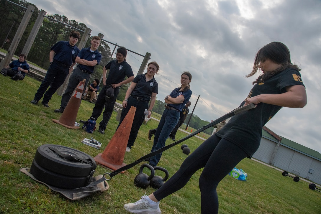 A high school student pulls a weighted sled while others watch