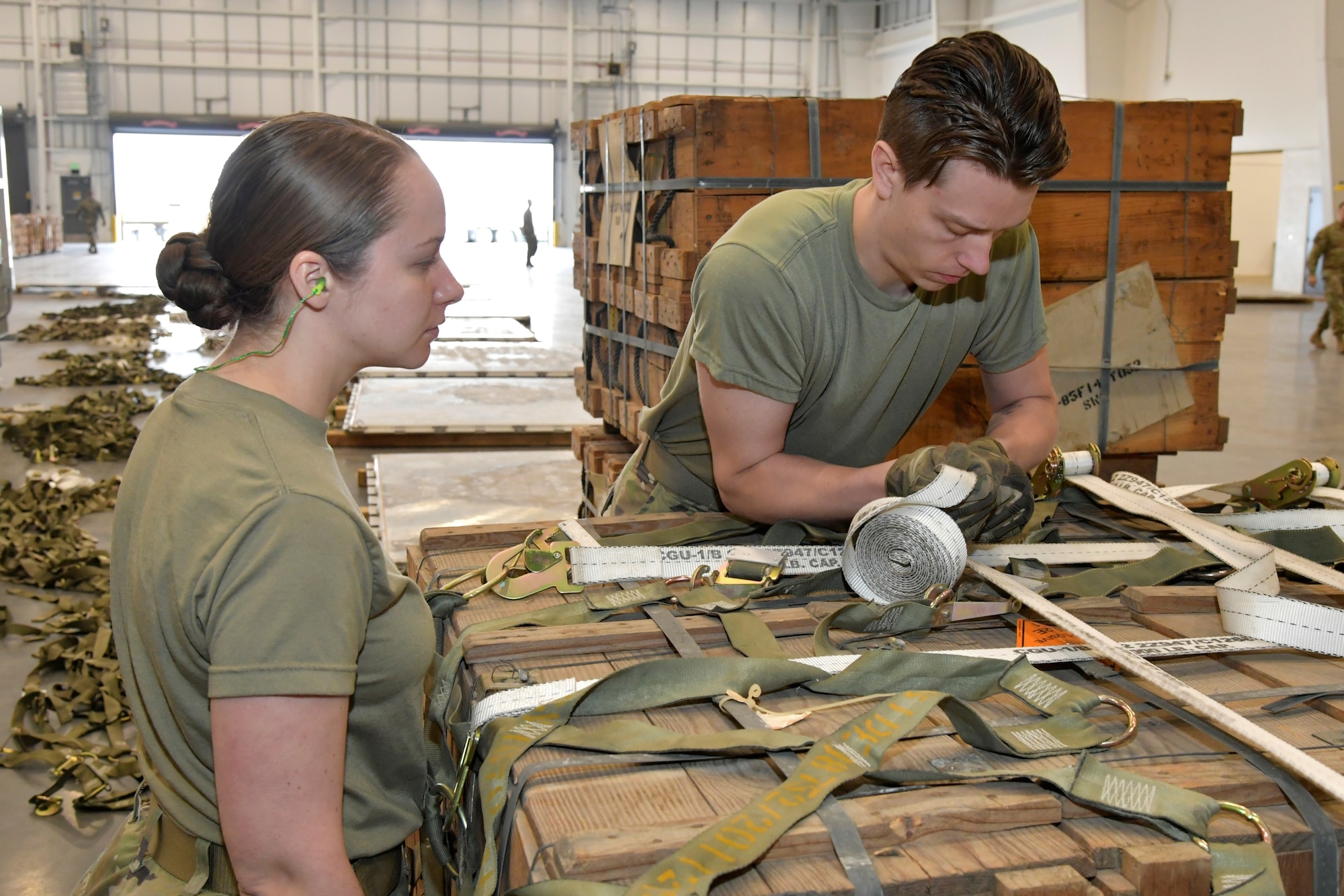 Two airmen secure tie-down straps on cargo netting