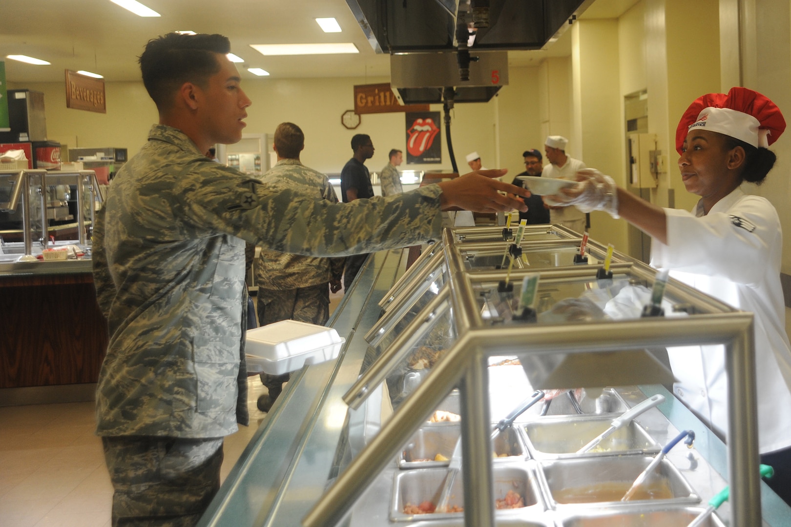 An airman receives a dish of food from a server.