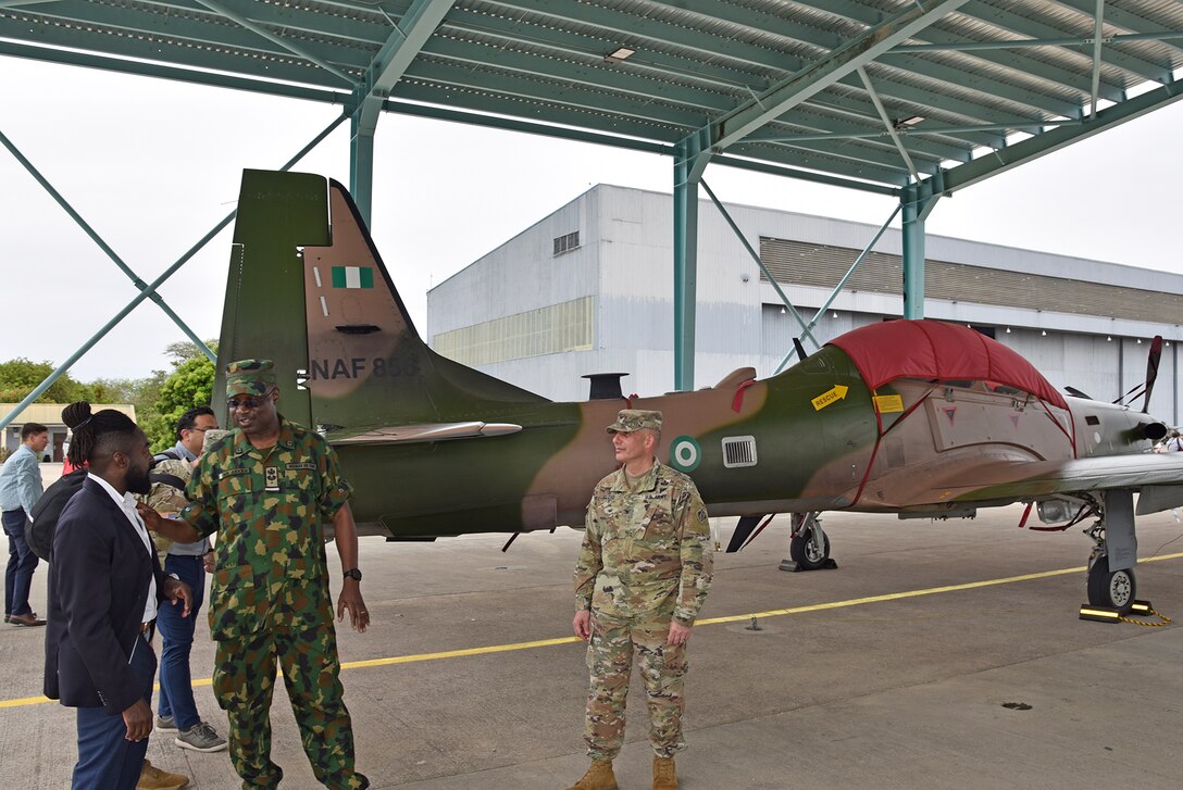 Three men speak near a military plane