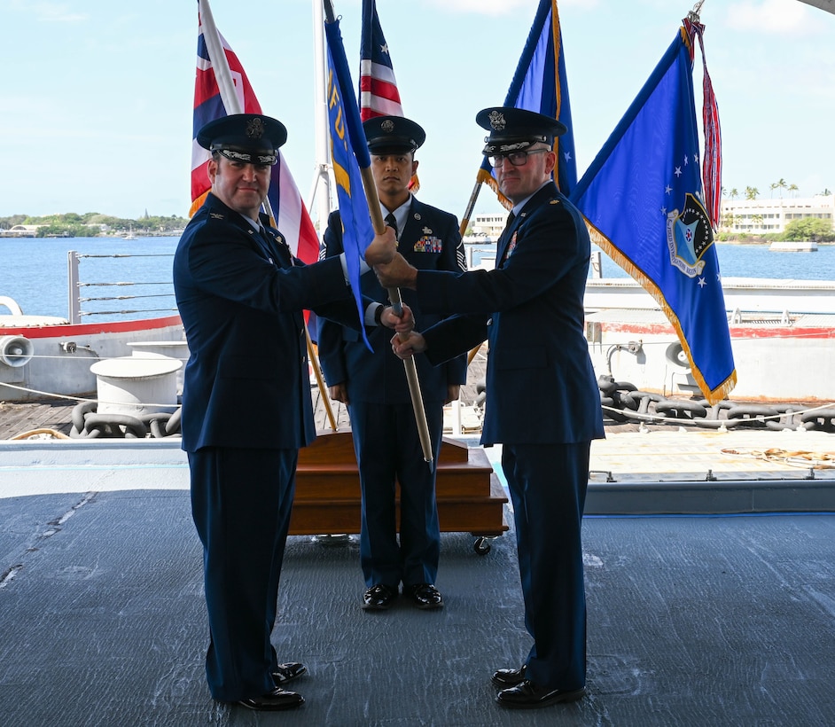 Maj. Michael J. Bryant accepts the guidon from OSI 6 FIR Commander, Col. Ben Hatch, during the assumption of command ceremony on board the battleship U.S.S. Missouri at Joint Base Pearl Harbor-Hickam, Hawaii, to standup the 13th Field Investigations Squadron, as 13 FIS Senior Enlisted Leader Rexor Domingo stands ready to assist March 30. (U.S. Air Force photo by SrA Zoie Cox, 15WG/PA)