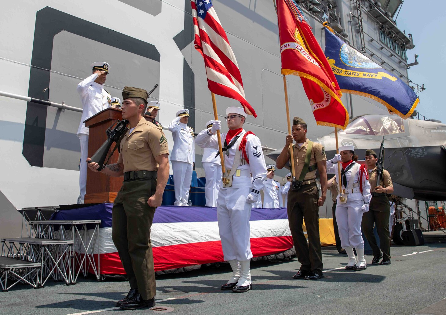 Sailors, and Marines assigned to the 13th Marine Expeditionary Unit (MEU) parade colors during a change of command ceremony on the flight deck of amphibious assault ship USS Makin Island (LHD 8), April 28, 2023 in the Philippines. The change of command ceremony is a time-honored naval tradition which formally proclaims the continuity and authority of command to the officers, men and women of the command. The Makin Island Amphibious Ready Group, comprised of Makin Island and amphibious transport dock USS Anchorage (LPD 23) and USS John P. Murtha (LPD 26), is operating in the U.S. 7th Fleet area of operations with the embarked 13th MEU to enhance interoperability with Allies and partners and serve as a ready-response force to defend peace and maintain stability in the Indo-Pacific region.