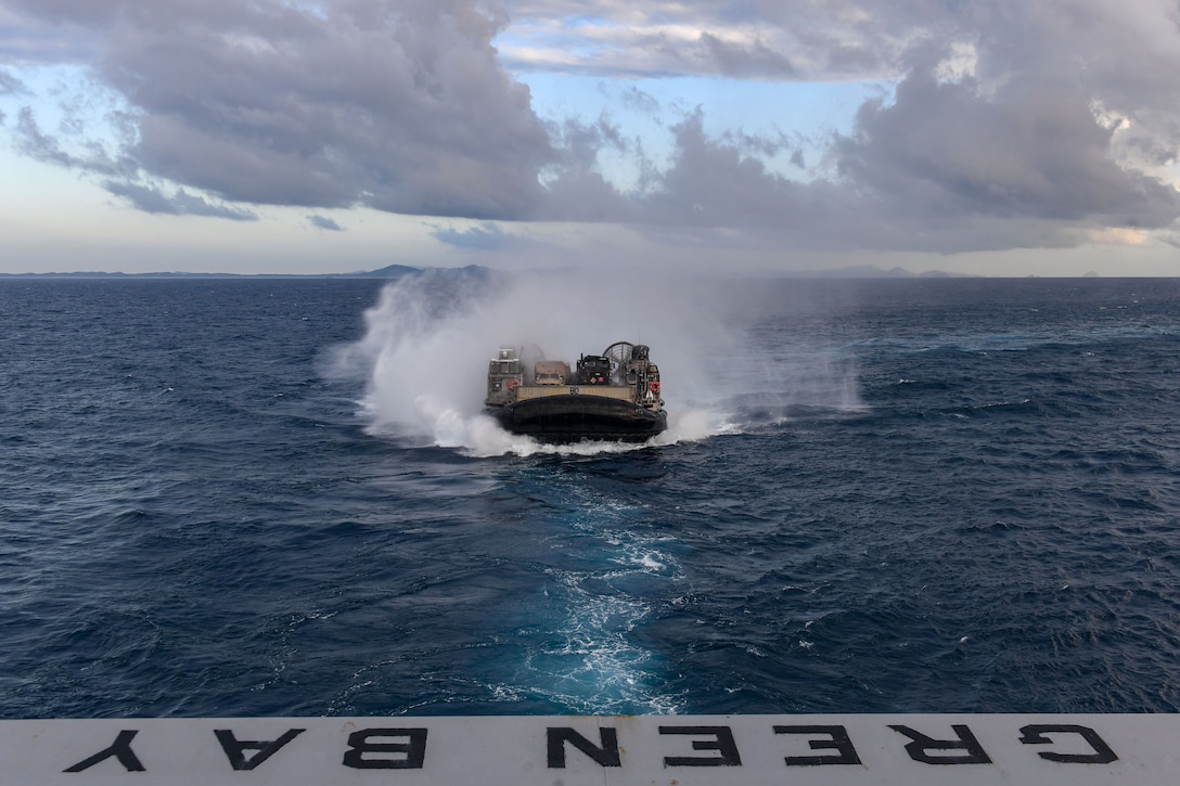 An  air cushioned landing craft arrives at the well deck of a large ship.