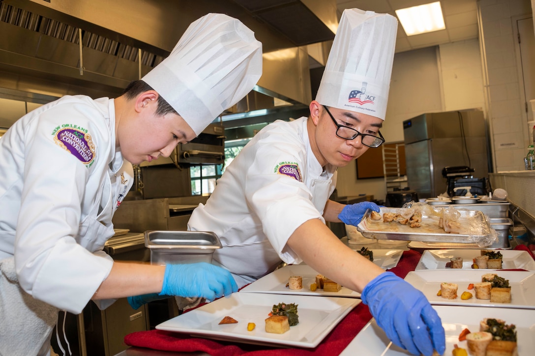 Two military chefs place food on multiple plates.