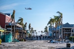 A Coast Guard Air Station Clearwater MH-60 Jayhawk flies overhead while personnel assigned to the Gulf, Atlantic, and Pacific Strike teams scan for unaccounted people in Fort Myers Beach, Florida on Sept. 29, 2022. Coast Guard National Strike Force teams mobilized to areas affected by Hurricane Ian to perform urban search and rescue. (U.S. Coast Guard photo by Petty Officer 3rd Class Gabriel Wisdom)