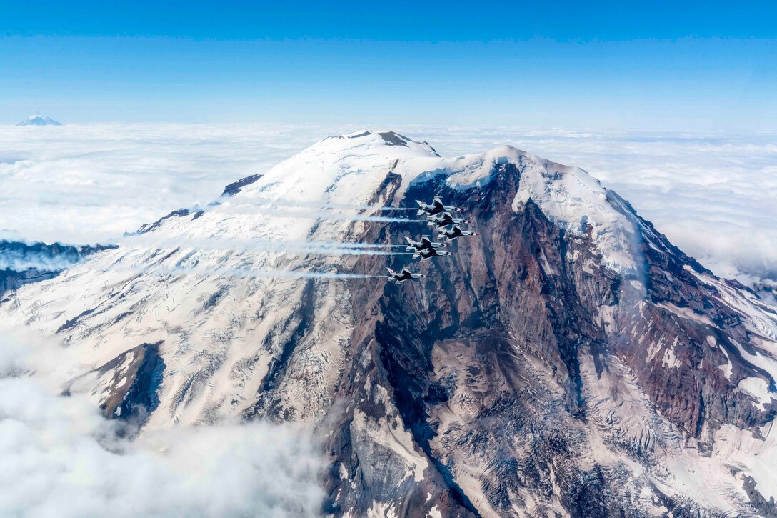 Aircraft fly in formation next to a snow-covered mountain.