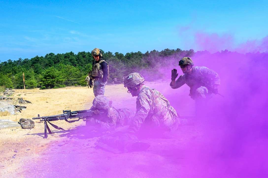 Soldiers participate in live-fire drills behind a cloud of purple smoke.