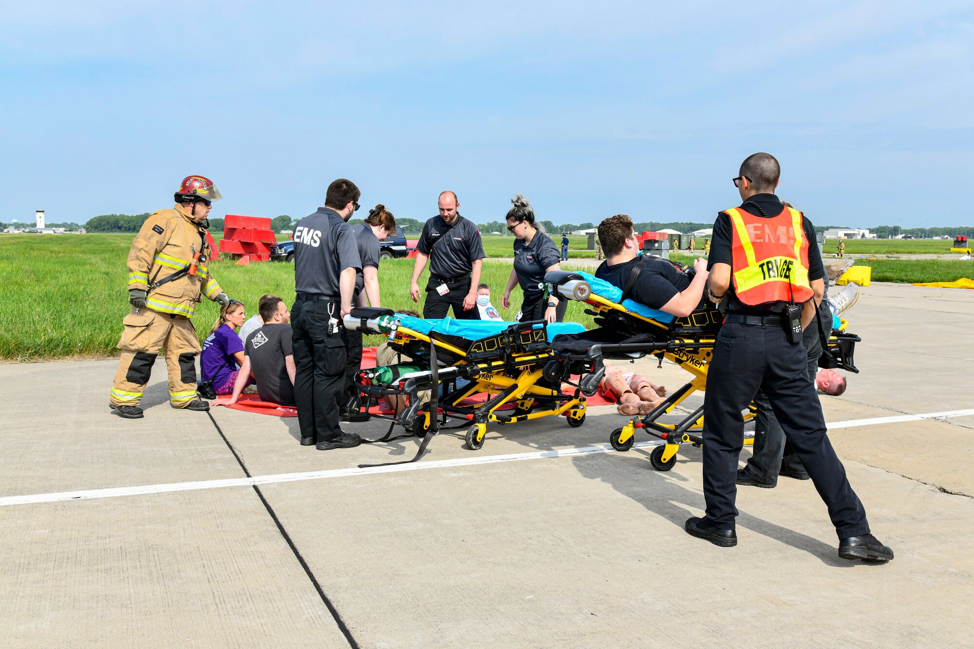 Group of uniformed Airmen and civilian paramedics with a gurney, practice responding to notional casualties.