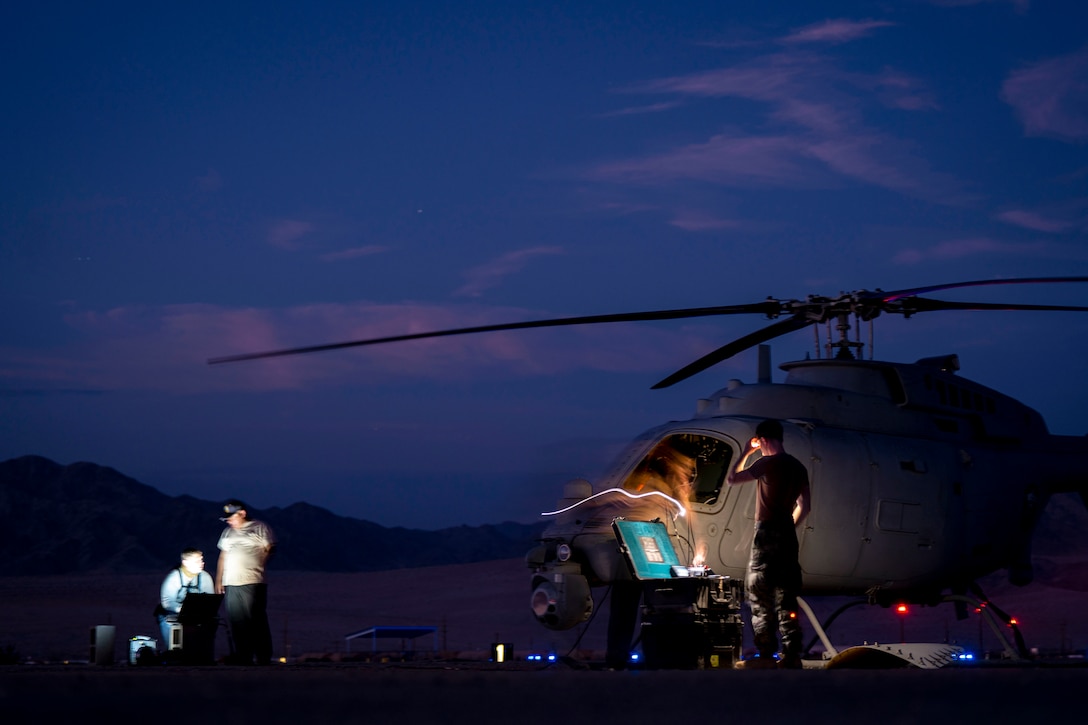 Service members work next to a parked helicopter in the dark illuminated by a streak of light.