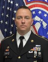 Male Soldier posing in front of U.S. flag and USAREC flag.