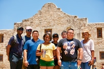 Nine Soldiers in civilian clothes pose for a photograph in front of The Alamo.