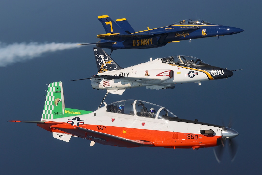 Three Navy aircraft fly in formation leaving behind a cloud of smoke.