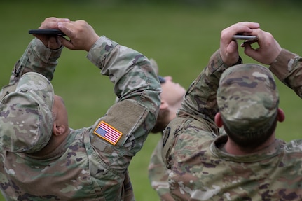 A pair of Alaska National Guardsmen use their phones to video Command Sgt. Maj. Michael Grunst parachute into his retirement ceremony July 21, 2023, at Camp Carroll on Joint Base Elmendorf-Richardson. Grunst joined the Alaska Army National Guard in 1989 and finished his 34-year career as the G3 operations sergeant major for the AKARNG.