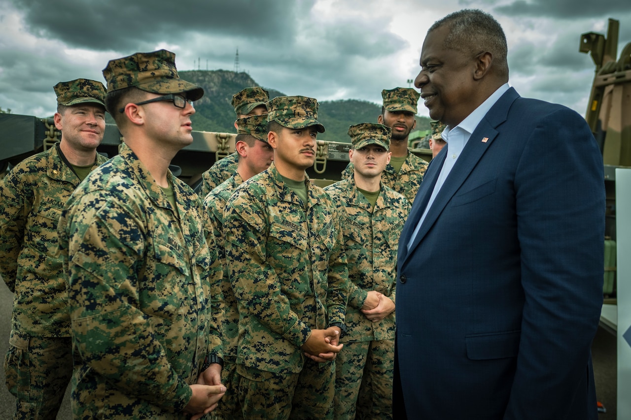 A man in a suit talks with U.S. Marines.