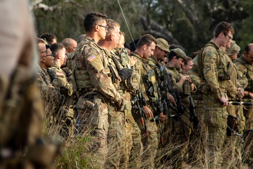 Soldiers from Comanche Company, 4th Battalion, 6th Infantry Regiment, listen to Talisman Sabre 23 opening remarks from the commander of Battle Group Ram in Townsville Field Training Area, Australia, July 21, 2023. The New Zealand and Australian army units performed a traditional war ritual following a group photo with partner nations assigned to Battle Group Ram for the exercise. Talisman Sabre is the largest bilateral military exercise between Australia and the United States advancing a free and open Indo-Pacific by strengthening relationships and interoperability among key Allies and enhancing our collective capabilities to respond to a wide array of potential security concerns. (U.S. Army photo by Sgt. Jason Greaves)