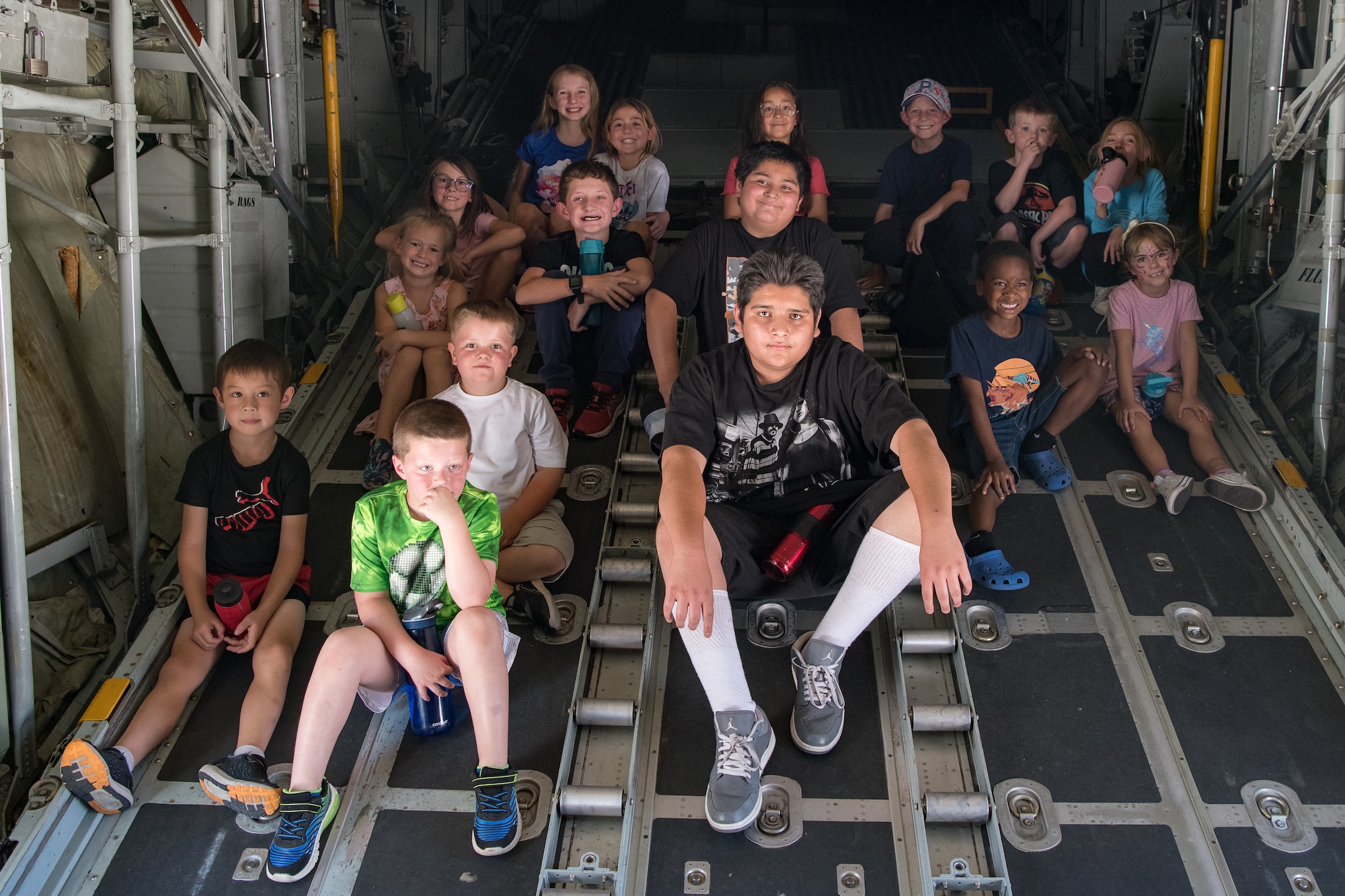 A group of children sitting on the closed cargo bay door of a C-130.