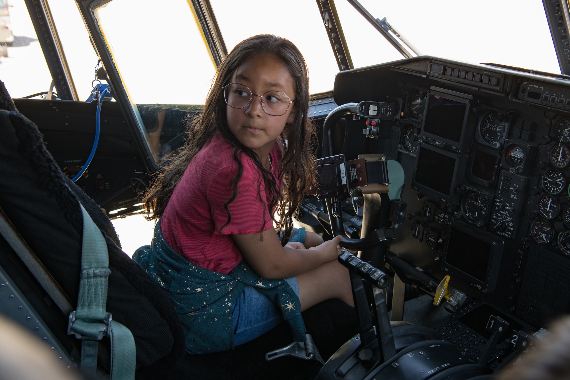 A child sits in a seat in the crew compartment of a C-130.