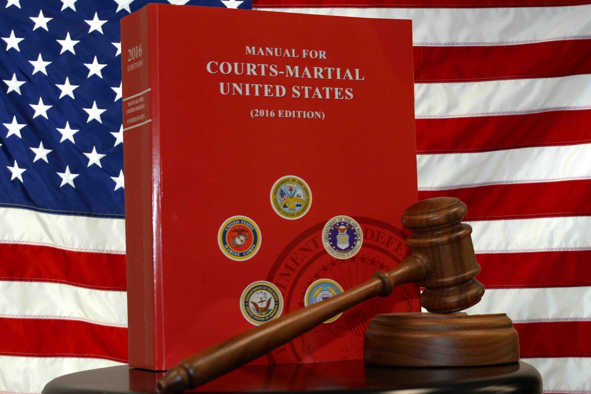 A wooden gavel and a large red book titled "Manual for Courts-Martial United States" are in front of a U.S. flag.